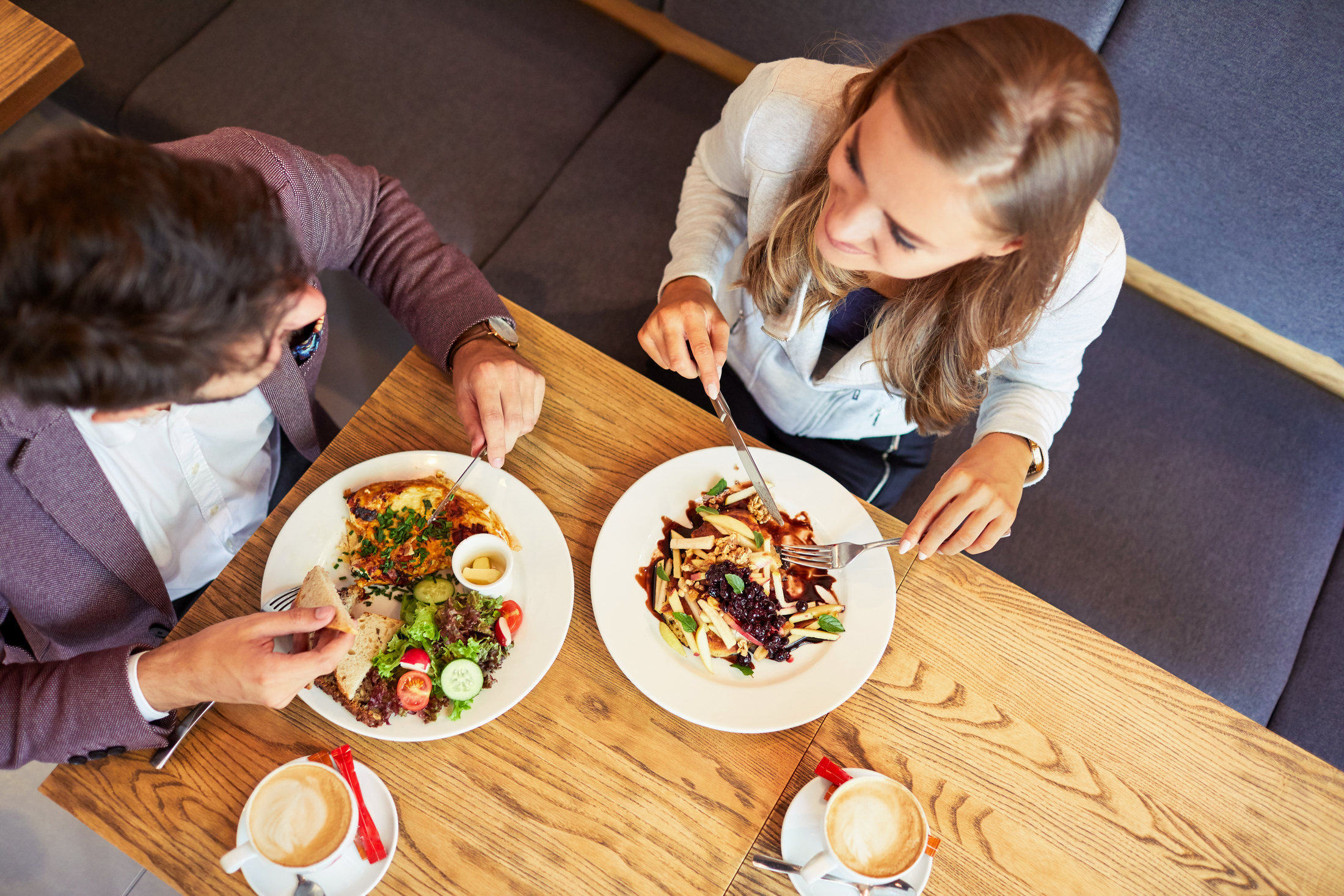 Zwei Personen essen Salat und trinken Kaffee an einem Tisch im großküchenähnlichen Speiseraum, aus der Vogelperspektive.