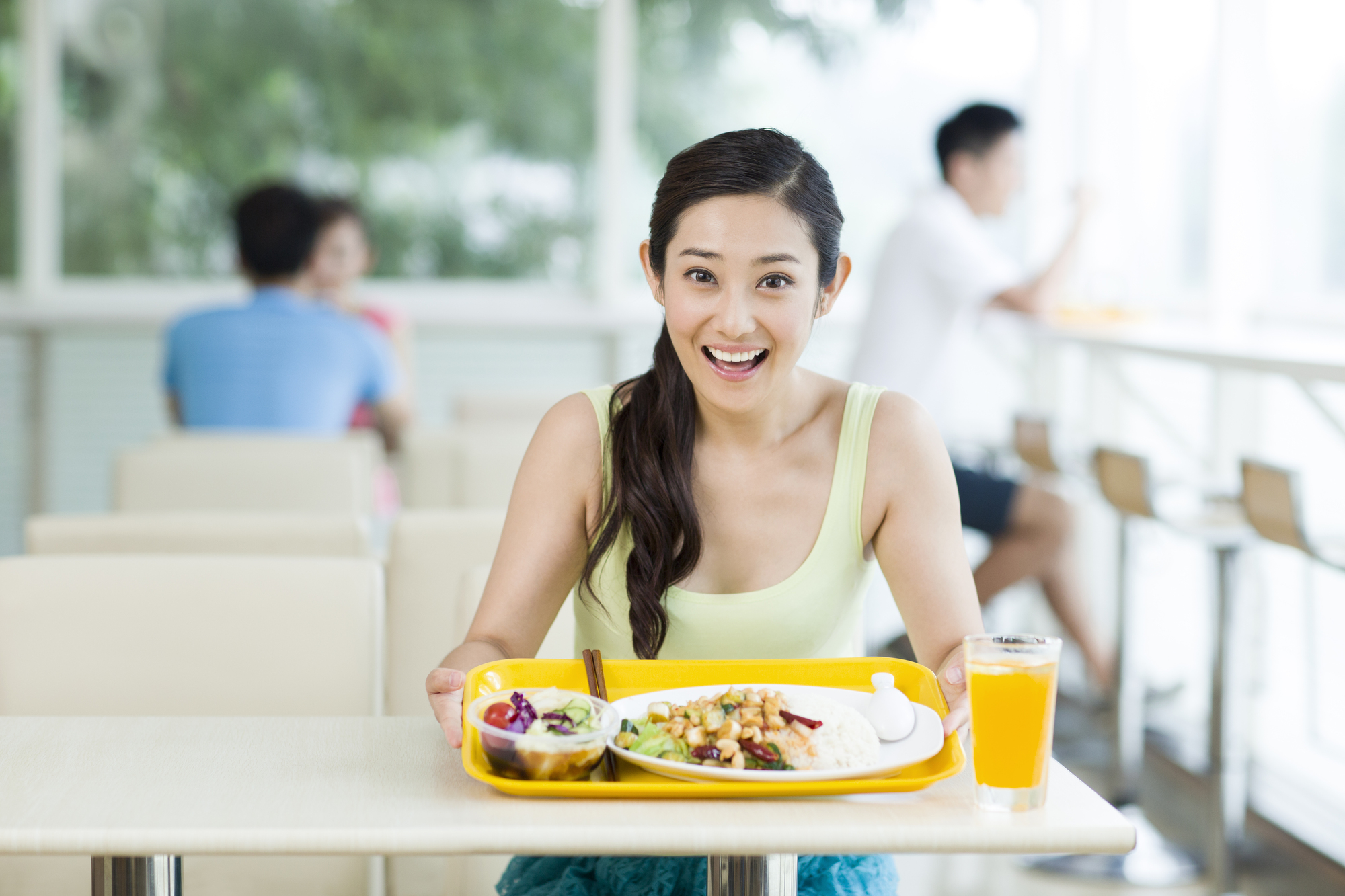 Frau isst eine Mahlzeit und trinkt Orangensaft in einem hellen, modernen Café mit Großküchen-Atmosphäre.