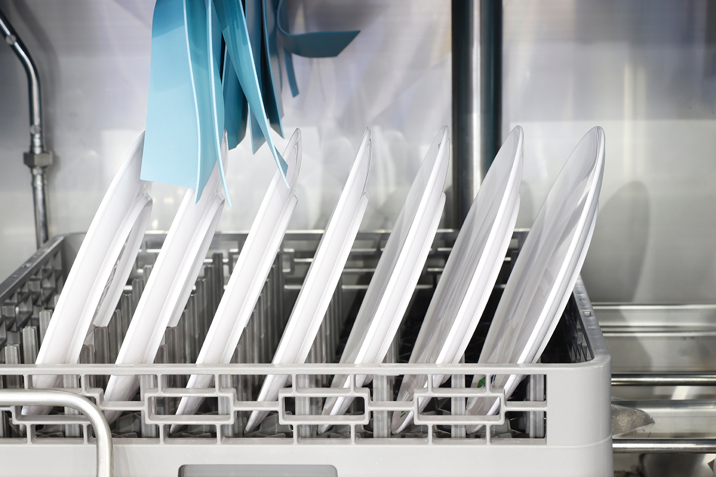 Geschirrspüler mit weißen Tellern und blauen Besteckteilen in einem Rack, umgeben von modernen Großküchengeräten.